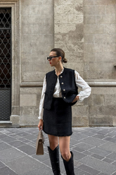 a lady in a white ruffle collared shirt, a black tweed vest and a black tweed skirt